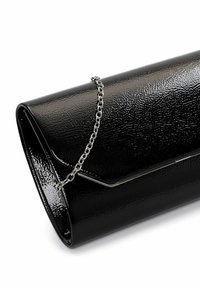 Pochette noire en cuir verni brillant avec bandoulière chaîne argentée, forme rectangulaire et fermeture à rabat sur fond blanc.