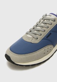 Blå och grå sneakers med övre i mocka och läder, med matchande snörning och en texturerad häl, märkt med "HUGO" på sidan.