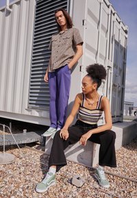 Camicia a maniche corte con stampa leopardata, pantaloni viola e sneakers verdi; modello seduto in pantaloni neri a zampa d'elefante e top in maglia a righe con dettagli.