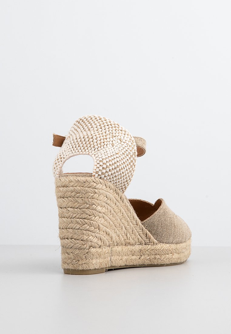 Beige Espadrille-Wedge mit strukturiertem Obermaterial und einem gewebten Riemen. Plattform aus Naturfasern mit abgerundetem Rücken und offenem Fersen-Design.