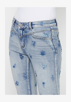 Jeans din denim de un albastru deschis, cu modele florale brodate în nuanțe de albastru. Prezentă un design clasic cu cinci buzunare și închidere cu nasture din metal.