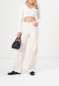 Vitt ribbat långärmad crop top, högmidjade krämfärgade vida jeans och en liten svart handväska med texturerad yta och korta handtag.