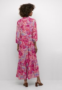 Pikk roosa kleit, millel on paisleimuster siniste ja lillade detailidega. Kleidil on pikad varrukad ja voolav aluslõige.