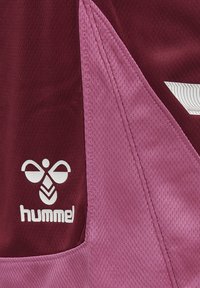 Bordeaux- och rosa sporttröja med texturerad tyg, snedställda färgpaneler och en vit "hummel"-logotyp med distinkta designelement.