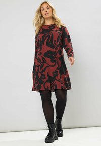 Langärmliges rotes Kleid mit schwarzem Blumenmuster, geripptem Bezug und gewelltem Saum, kombiniert mit schwarzen Schnürstiefeln.