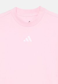 Lys rosa bomull t-skjorte med rund hals og en liten hvit Adidas-logo på brystet, med glatt tekstur og minimalistisk detaljer.