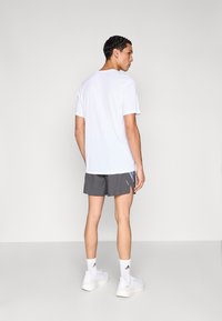 Valkoinen lyhythihainen paita, harmaat urheilushortsit sinisillä yksityiskohdilla, valkoiset lenkkitossut ja valkoiset urheilusukat. Takakuvassa asu.