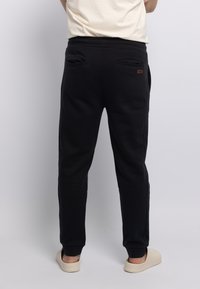 Zwarte sweatpants met een slim fit, met achterzakken en elastische boorden. Het materiaal is zacht met een gladde textuur. Accentuatie met logodetail aanwezig.