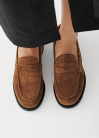 Καφέ δερμάτινα loafers με στρογγυλεμένη μύτη, ραμμένες λεπτομέρειες, ανυψωμένη γλώσσα και μαύρη καουτσούκ σόλα, τοποθετημένα πάνω σε απλό λευκό φόντο.
