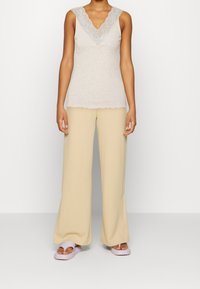 Débardeur gris clair avec un col en V en dentelle, associé à un pantalon large crème et des chaussures à enfiler lilas clair, présentant une texture lisse.