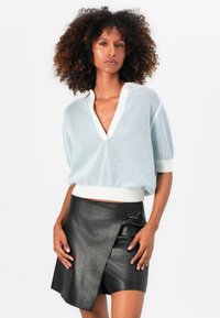 Himmelblauer Netzpullover mit V-Ausschnitt und kurzen Ärmeln. Kombiniert mit einem schwarzen Lederwickelrock mit seitlichem Akzent.