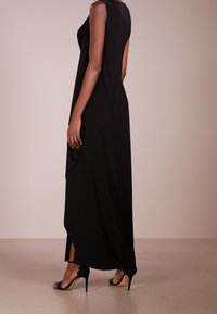 Svart ärmlös maxiklänning med en flödande design, med sidoklyftor och en mjuk textur, ihop med svarta högklackade skor.