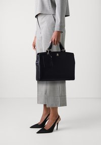 Borsa a tracolla in pelle nera con manici corti, dotata di un portacarte rimovibile e accessori in argento. Abbinata a un completo a righe in due pezzi.