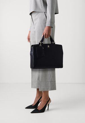 Borsa a tracolla in pelle nera con manici corti, dotata di un portacarte rimovibile e accessori in argento. Abbinata a un completo a righe in due pezzi.