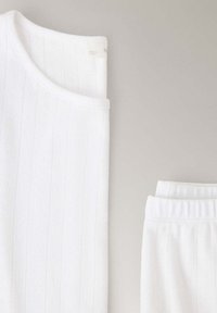 Débardeur blanc côtelé sans manches et short côtelé assorti posés à plat sur une surface claire.
