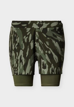 Shorts de sport à motif camouflage vert et foncé avec des leggings de compression verts unis attachés en dessous, présentés sur un fond uni.