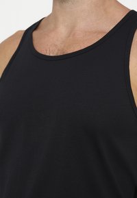 Primo piano di una persona che indossa una canottiera nera senza maniche, mostrando la parte superiore del petto e del collo con leggera peluria sul petto.