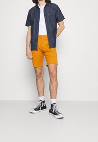 Mörkblå kortärmad skjorta, vit t-shirt under, orange shorts och svarta sneakers med vita sulor. Avslappnad outfit med en ledig passform.