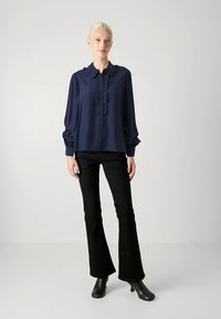 Tumši zila blūze ar volānu apkaklīti un priekšpusi, plūstošām piedurknēm un pogu aizdari. Savienota ar melnām izplatītām biksēm un potīšu zābakiem.