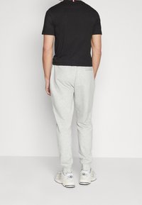 Camiseta negra de manga corta, pantalones deportivos grises y zapatillas blancas. La camiseta tiene una banda de contraste de color en la parte trasera. Tela de algodón suave.