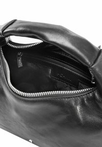 Wnętrze czarnej skórzanej torebki z zamykaną na suwak kieszenią i gładką fakturą z srebrnymi okuciami. Podszewka jest ciemna, co poprawia widoczność.