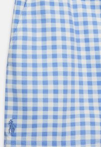 Světle modrá a bílá kostkovaná tkanina s texturovaným povrchem. Obsahuje malé vyšívané logo postavy v modré barvě v dolním levém rohu.