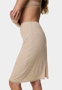 Beżowa spódnica ołówkowa wykonana z gładkiego materiału o subtelnym połysku. Posiada falbaniasty koronkowy dół oraz boczny rozporek dla większej swobody ruchów.