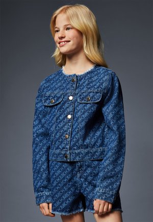 Veste en denim bleue avec un motif texturé, dotée de boutons dorés, de deux poches poitrine et d'un ourlet effiloché. Associée à un short en denim assorti.