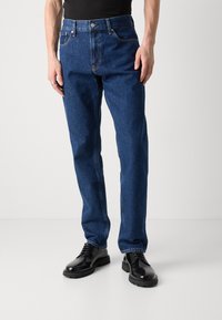 Tumedat sinised teksapüksid sirge lõikega, viie tasku ja nähtava õmblusega, klassikalise nööbi ja lukuga sulgemine.