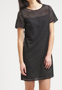 Vestido negro de corte holgado, con un patrón de malla texturizada, mangas cortas y escote redondo.