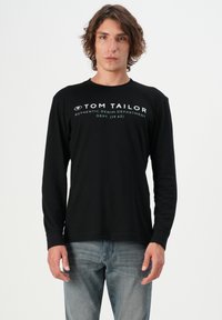 Pikad varrukad must t-särk valgete tähtede, sealhulgas "TOM TAILOR" ja "AUTHENTIC DENIM DEPARTMENT", valmistatud pehmest kangast.