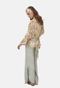 Top con estampado floral en rosa y verde, con mangas largas y un lazo en la cintura. Pantalones de pierna ancha en verde claro con aberturas laterales y detalles de ribete.
