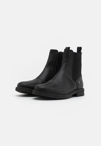 Bottes basses en cuir noir avec panneaux latéraux élastiques et une languette à l'arrière. Dotées d'une semelle en caoutchouc durable et d'une texture lisse.