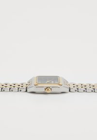 Montre carrée avec un cadran noir, des accents dorés et un bracelet en acier inoxydable argenté. Dotée d'une lunette polie et d'une couronne poussoir.