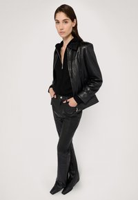 Giacca di pelle nera con zip frontale, abbinata a un top nero aderente e pantaloni in pelle svasati. Texture liscia e vestibilità sagomata lungo tutto l'outfit.