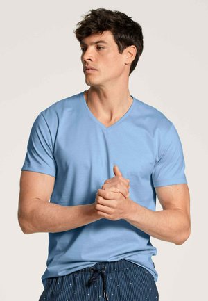 T-shirt azzurro a maniche corte con scollo a V, realizzato in tessuto morbido, caratterizzato da una vestibilità rilassata e una texture liscia. Indossato con pantaloni corti a fantasia.