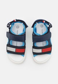 Tummansiniset ja vaaleansiniset taaperon sandaalit, joissa on valkoisia ja punaisia raidoituskoristeita, tarranauhat ja valkoiset teksturoidut pohjat, koko 24.