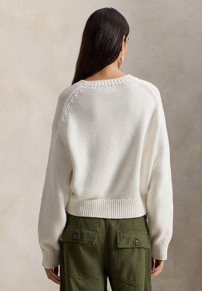 Λευκό πουλόβερ πλεκτό με υφή, σε κοντό μήκος, με ριμπ τελείωμα και πεσμένους ώμους, συνδυασμένο με χακί cargo παντελόνι που έχει πίσω τσέπες.