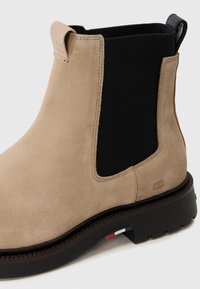 Botină Chelsea din suede bej cu panouri elastice laterale negre, mâner și detaliu stripe contrastant pe talpă. Talpă din cauciuc rezistentă.