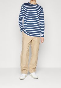 Langärmliges navy- und weißgestreiftes T-Shirt, kombiniert mit beigen Cargo-Hosen, die seitliche Taschen und weiße Sneaker aufweisen. Glattes Baumwollmaterial.