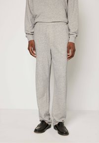 Sive pletene trenirke z elastičnim pasom in ravnim krojem, v kombinaciji s črnimi loaferji, na beli podlagi.