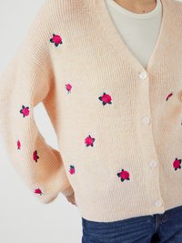 Cardigan en tricot côtelé pêche avec broderie de roses roses, décolleté en V et six boutons sur le devant. Coupe ample avec des manches larges.