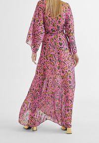 Lång, genomskinlig klänning i en livlig rosa färg med leopardmönster, som har gröna och gula accenter, breda ärmar och en åtsittande midja.