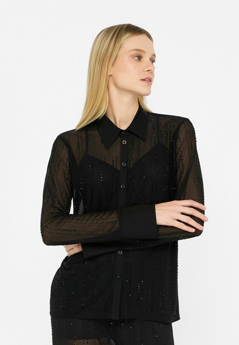 Blouse noire transparente avec un devant à boutons, manches longues, texturée avec des lignes verticales et de petits embellissements, dotée d'un col classique.
