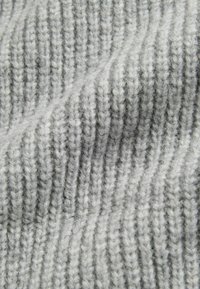 Tessuto tricot grigio con texture a righe verticali. Il filato appare morbido, presentando un colore grigio chiaro con leggere variazioni di tonalità.