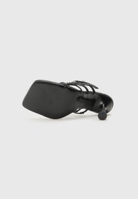 Sandale à talon noir avec un bout carré, des brides fines, une semelle texturée et un talon aiguille étroit pour plus de hauteur.