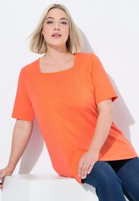 Top naranja de manga corta con escote cuadrado, hecho de material suave. Presenta un corte relajado y una textura lisa, acompañado de jeans azules.