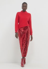 Pull rouge en tricot avec un col montant, associé à une jupe en sequins rouge longue jusqu'au sol et des bottines rouges. Texture lisse avec des accents brillants.