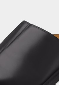 Κοντινή όψη ανώτερου μέρους μαύρου δέρματος με λεία υφή που δείχνει λεπτομερή ραφές και μέρος της σόλας.