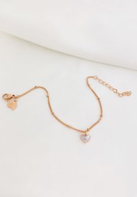 Bracciale a catena in oro rosa con un ciondolo a forma di cuore con un'inserzione di pietra bianca e un ulteriore piccolo ciondolo a forma di foglia.